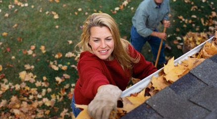 photo: woman cleaning leaves from the gutters of a house